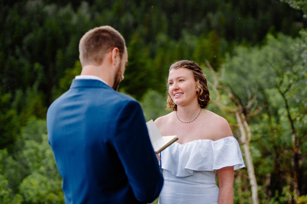 bride smiling at groom as he reads his marriage vows during their eldora mountain colorado elopement 