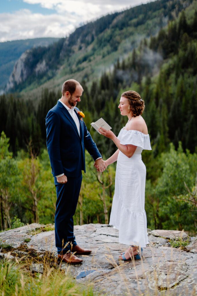 bride holding grooms hand as she reads her marriage vows on top of a mountain at her family cabin at their eldora mountain colorado elopement