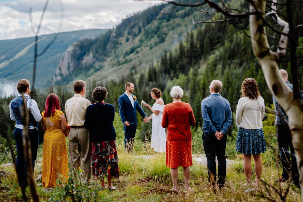 bride and groom holding hands reading their vows to each other on top of a mountain surronded by their families during their eldora mountain colorado elopement