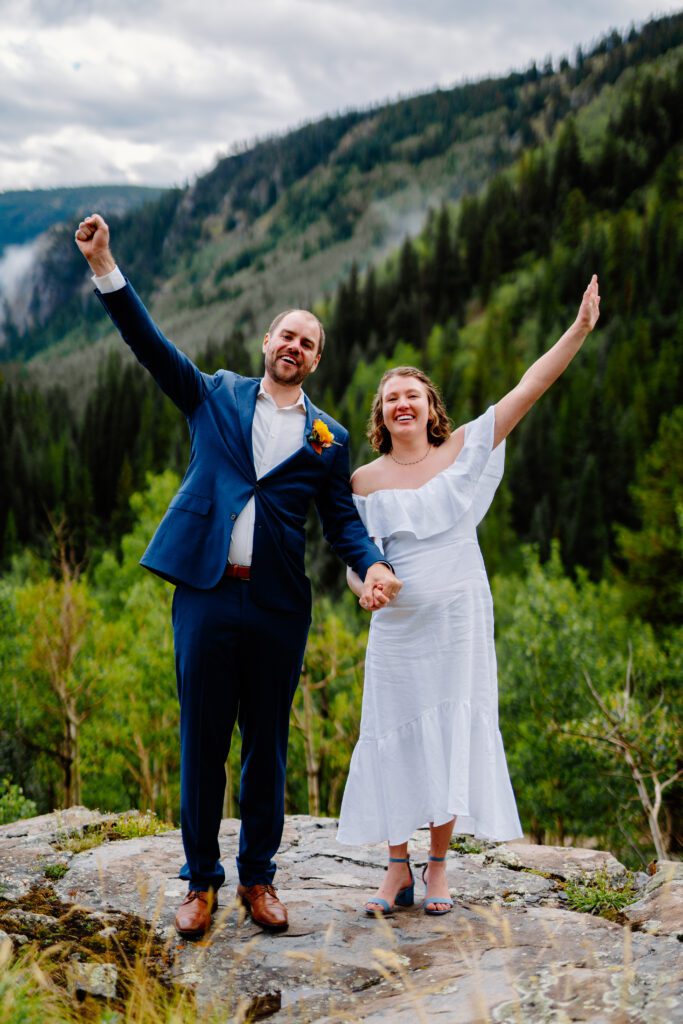 bride and groom holding hands and cheering after making their marriage official on top of a mountain in eldora colorado