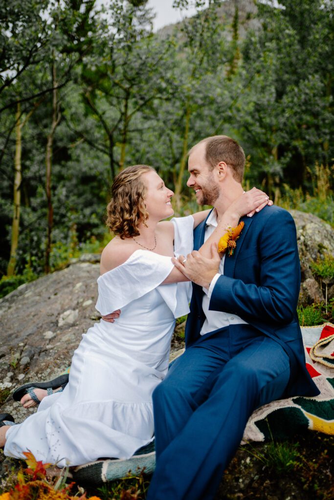bride throwing her arms around grooms neck as they sit on a rock during their eldora mountain colorado elopement