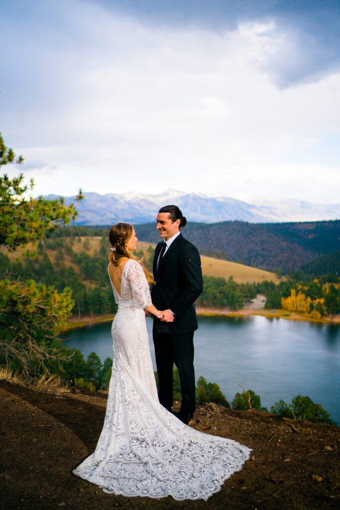 bride and groom holding hands on the side of a cliff overlooking an alpine lake during their colorado springs elopement