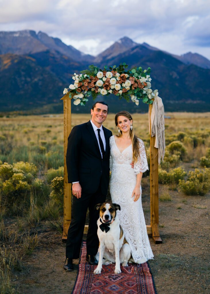 bride, groom and their dog smiling at the camera at the arbor during their colorado springs elopement