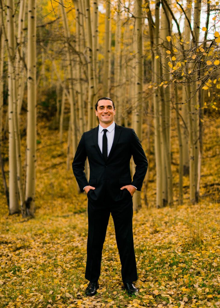 groom standing in a grove of aspens smiling at the camera during his colorado springs elopement