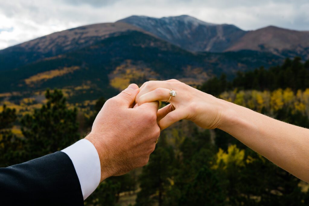 groom and bride holding hands zoomed in on the ring with the mountain peak in the background during their colorado springs elopement
