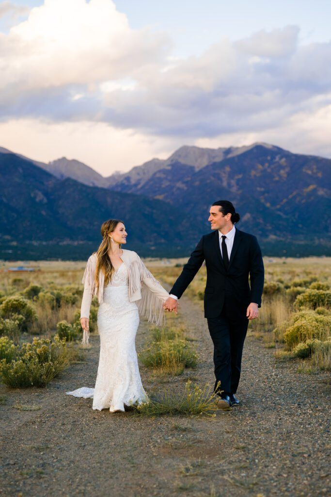 bride and groom holding hands and walking down a path together in crestone colorado during their colorado springs elopement