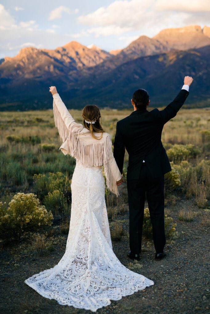 bride and groom holding hands facing away from the camera with fist pumps during their colorado springs elopement
