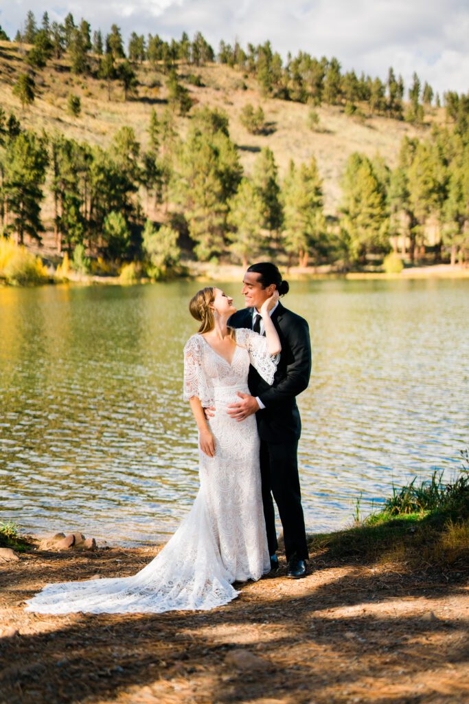 bride and groom smiling at each other on the shore of a lake during their colorado springs elopement