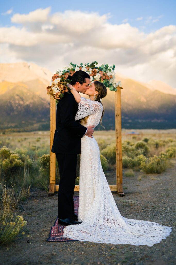 bride and groom kissing in front of the arbor with the mountains in the background during their colorado springs elopement