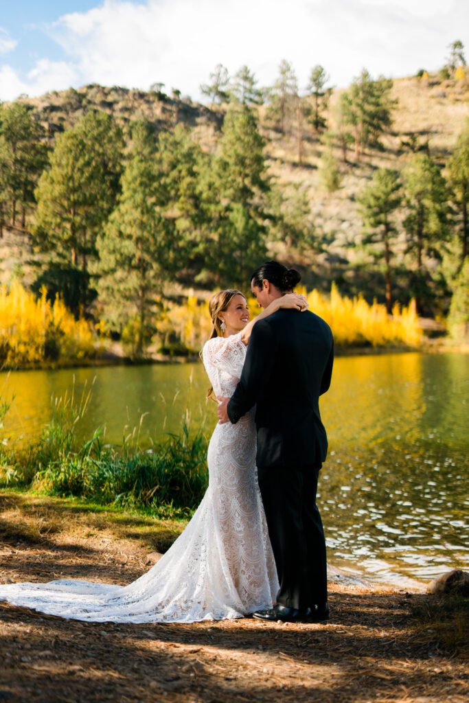 bride with arms around the grooms neck smiling up at him on the shore of a lake during their colorado springs elopement