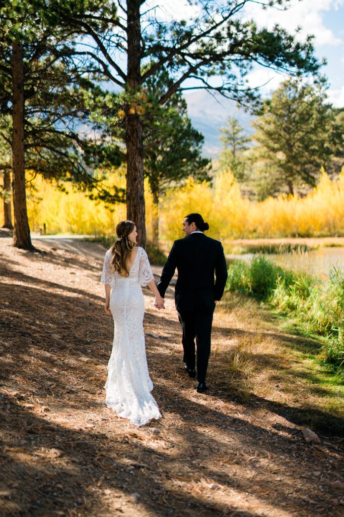 bride and groom holding hands smiling at eachother and smiling while walking along the lake shore during their colorado springs elopement