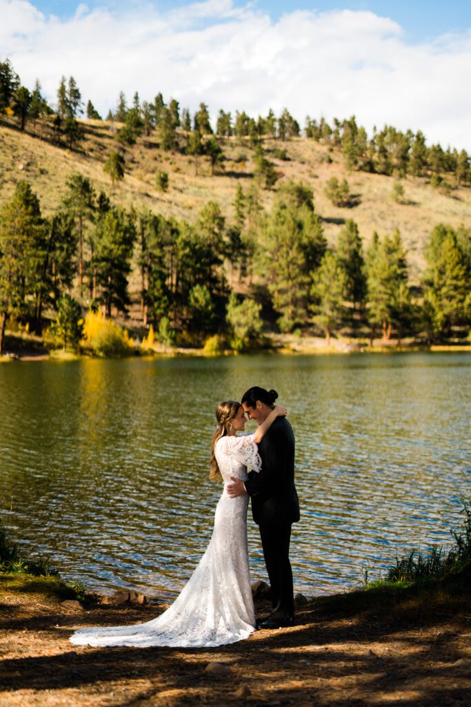 bride and groom standing on the shore of a lake nose to nose smiling at each other during their colorado springs elopement