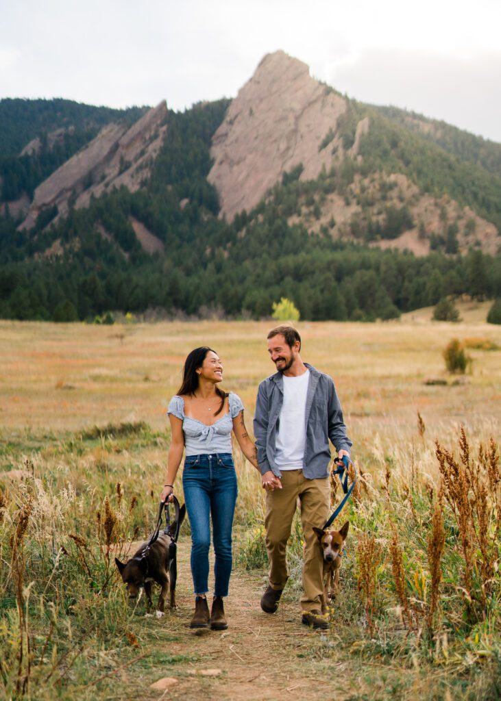 engaged couple walking their dogs in a field during their Chautauqua Park Engagement Photos
