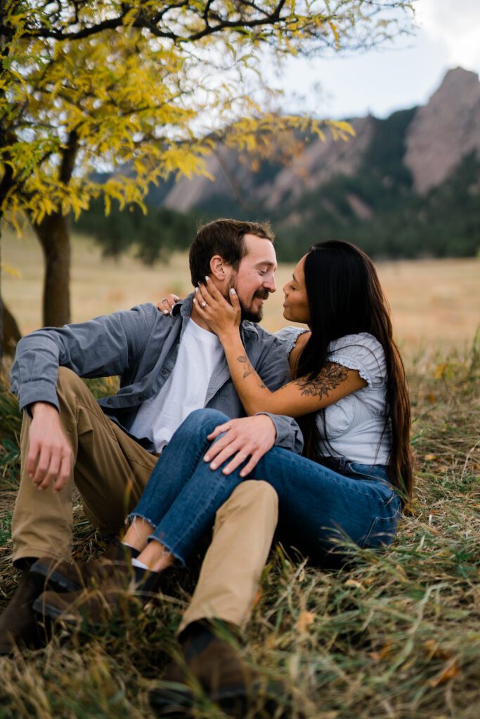 engaged couple sitting in a field at Chautauqua park during their engagement photos