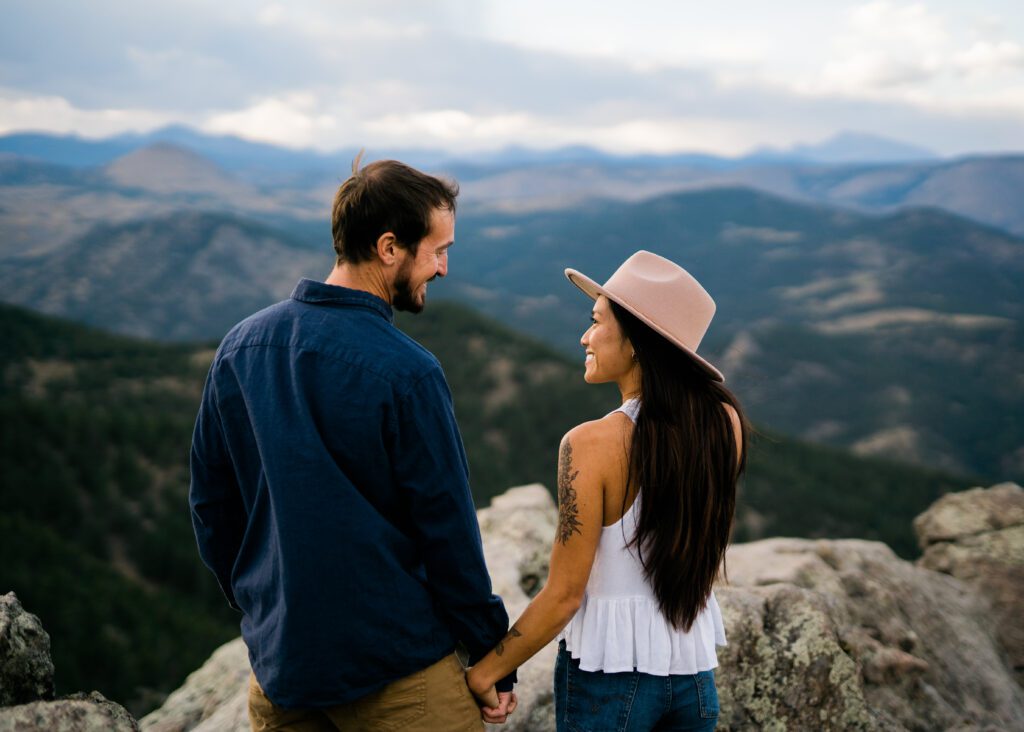 couple holding hands smiling at eachother while looking out at the mountains during their Chautauqua Park Engagement Photos