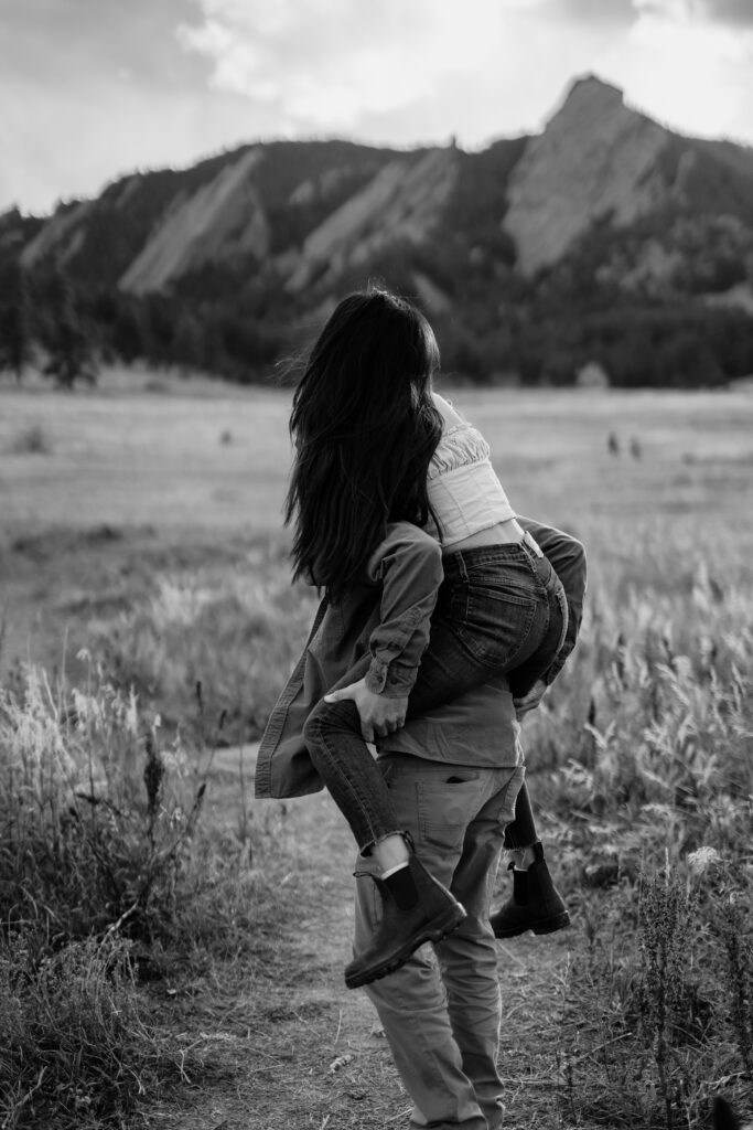 fiance giving his girlfriend a piggyback ride in a field in boulder colorado during their Chautauqua Park Engagement Photos