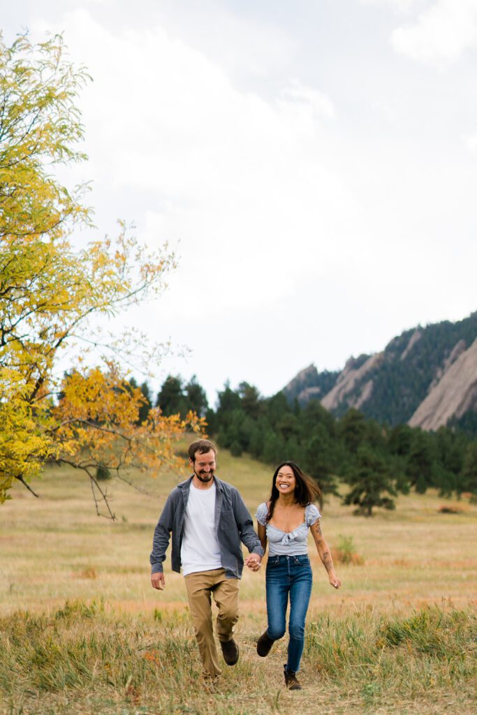 engaged couples running in the field in boulder Colorado during their Chautauqua Park Engagement Photos
