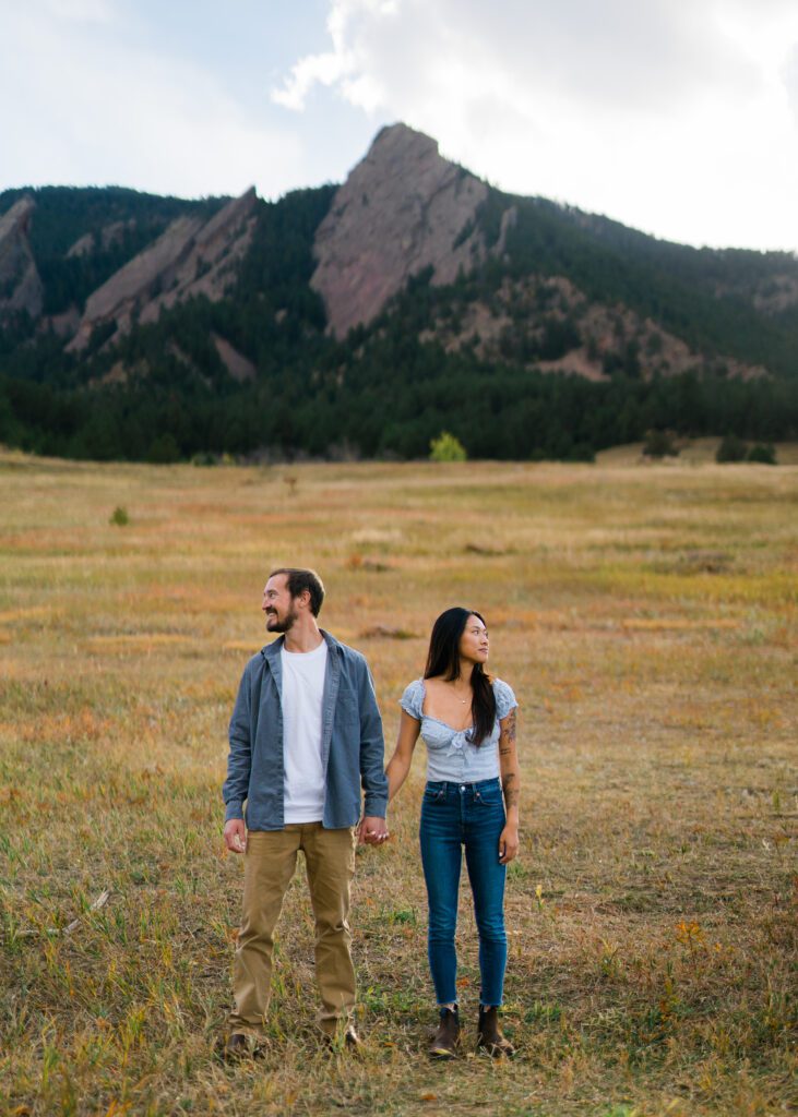 engaged couple holding hands at the base of the flat irons in boulder colorado during their Chautauqua park engagement photos