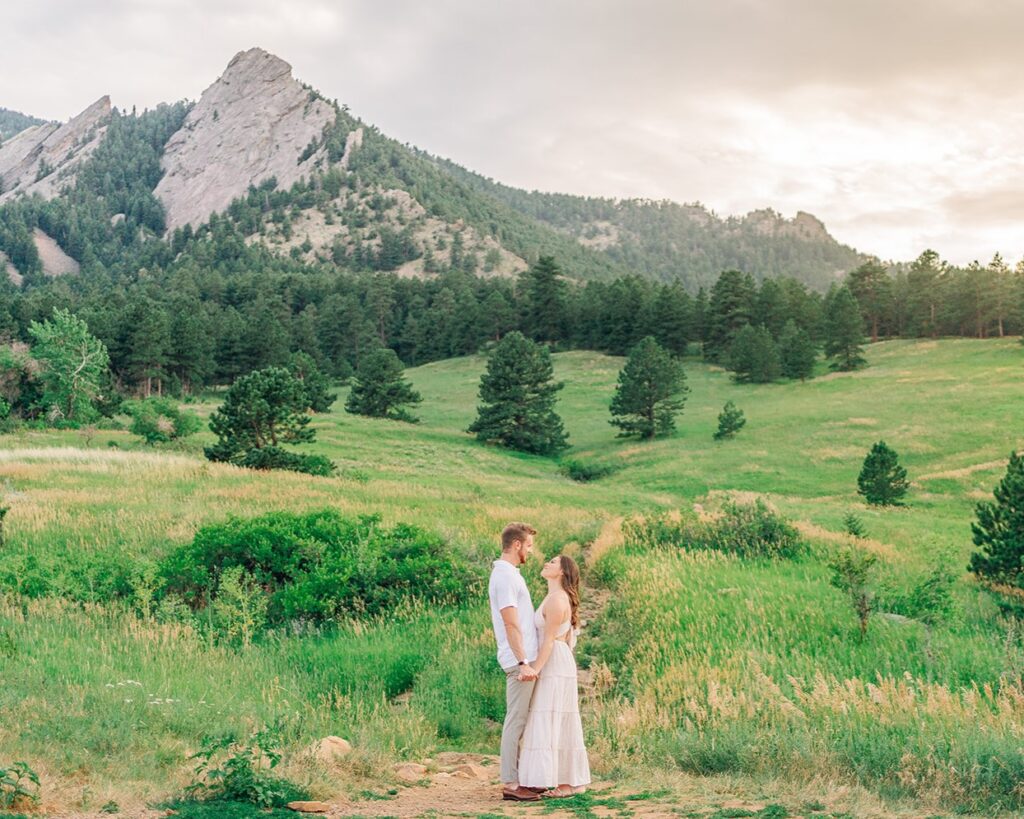 cute couple holding hands in front of the boulder colorado flatirons during their couples session at chautauqua park