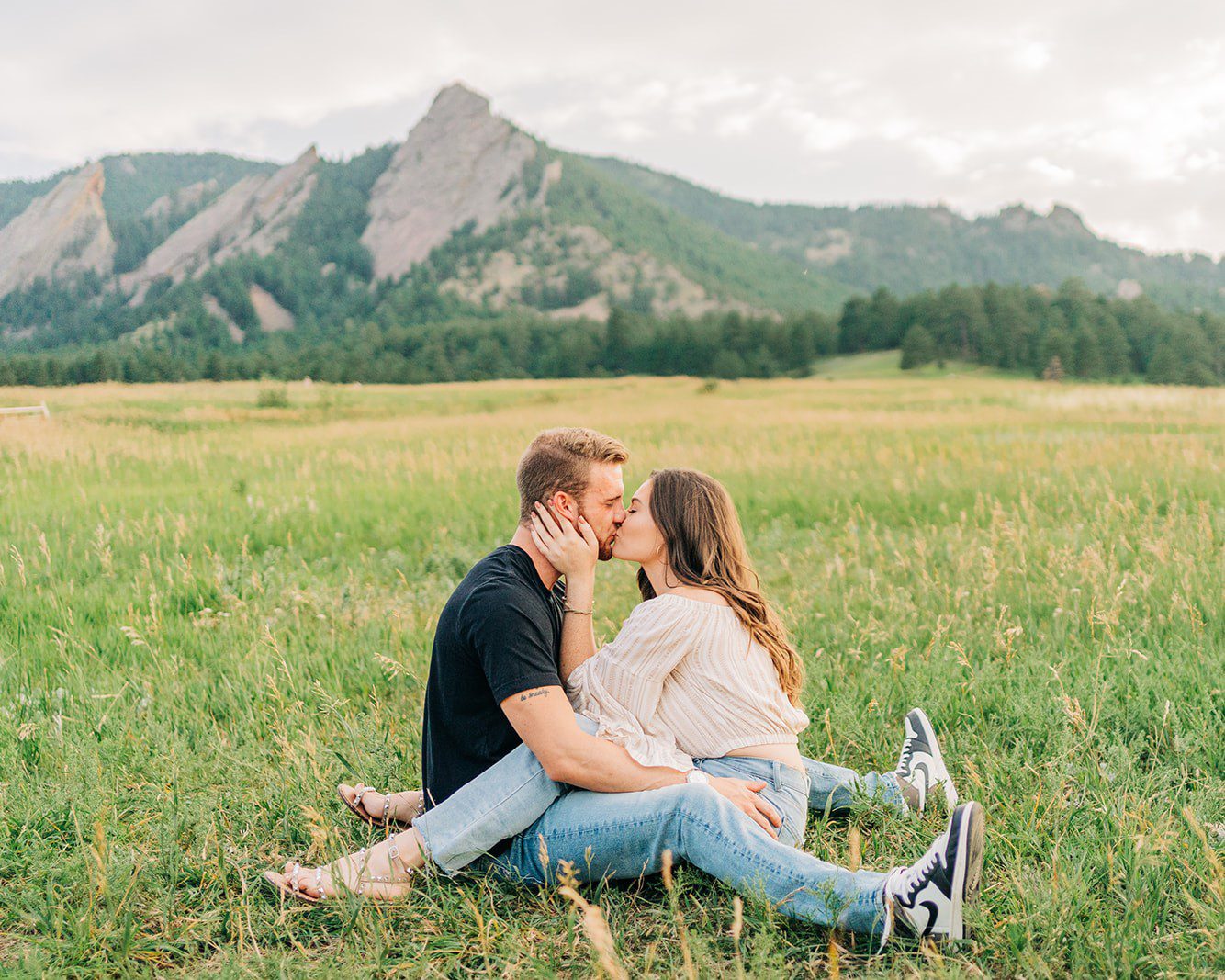 Cute engaged couple sitting in front of the flatirons in boulder colorado during their couples photoshoot at chautauqua park