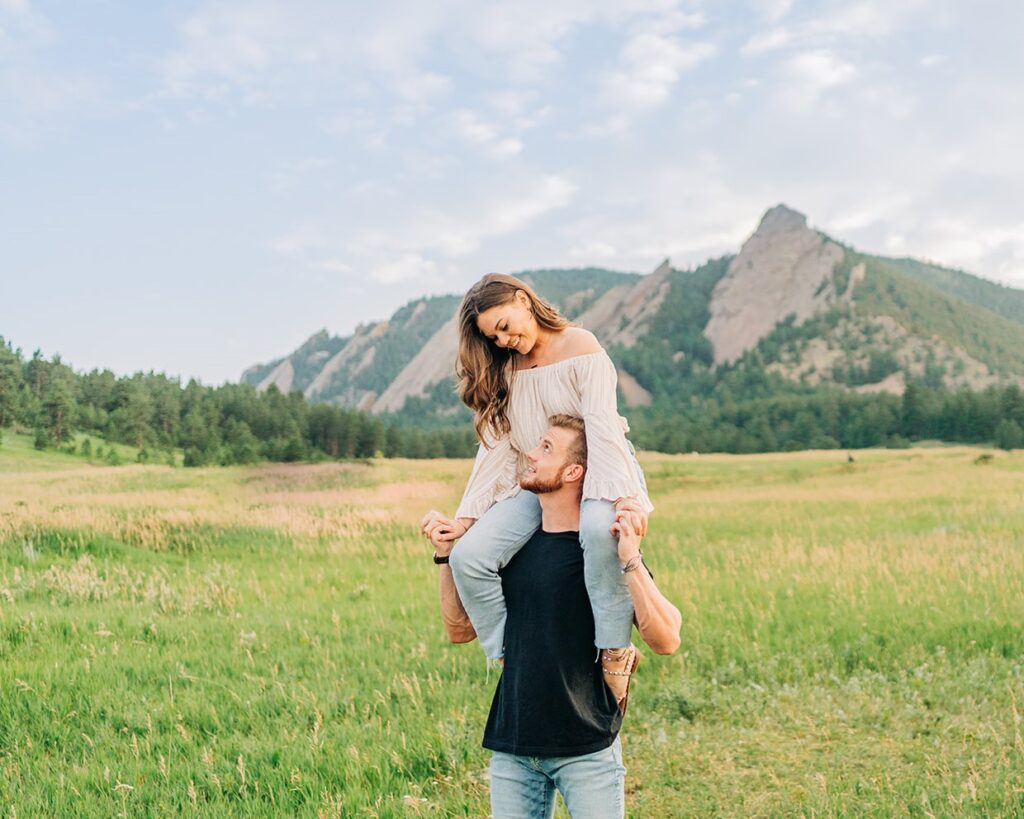 boyfriend giving his girlfriend a shoulder ride in front of the flatirons during their boulder colorado coouples photoshoot at chautauqua park