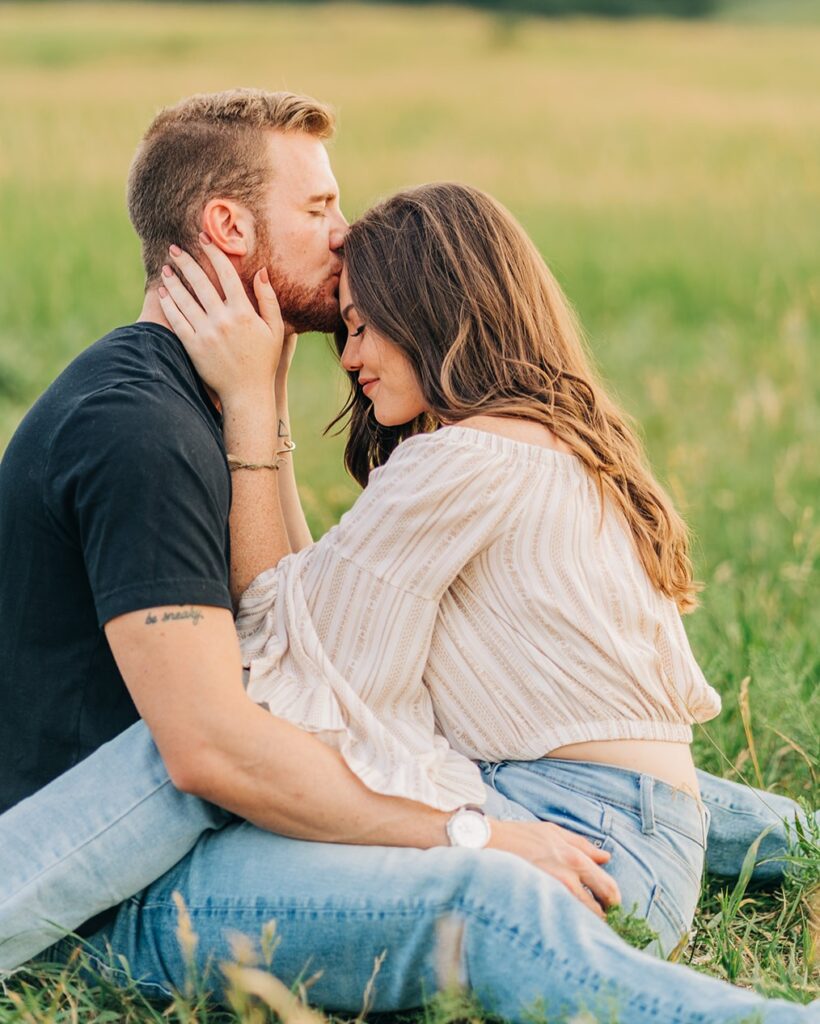 boyfriend kissing his girlfriends forehead as they sit in a field at chautauqua park during their boulder colorado couples session
