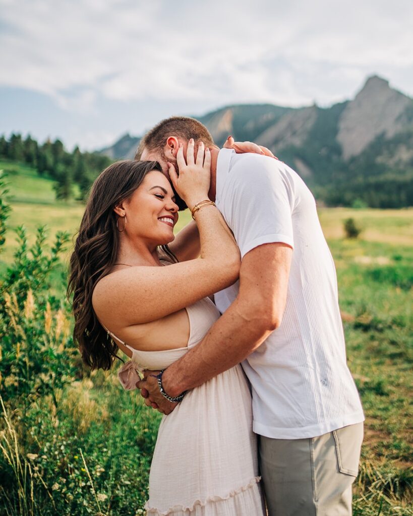 girlfriend holding her boyfriends face while he kisses her on the cheek at the flatirons during their boulder colorado couples session at chautauqua park