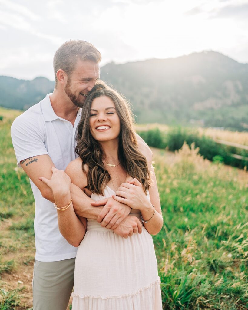 boyfriend kissing his girlfriend on the forehead while she smiles at the camera during their boulder colorado couples session at chautauqua park