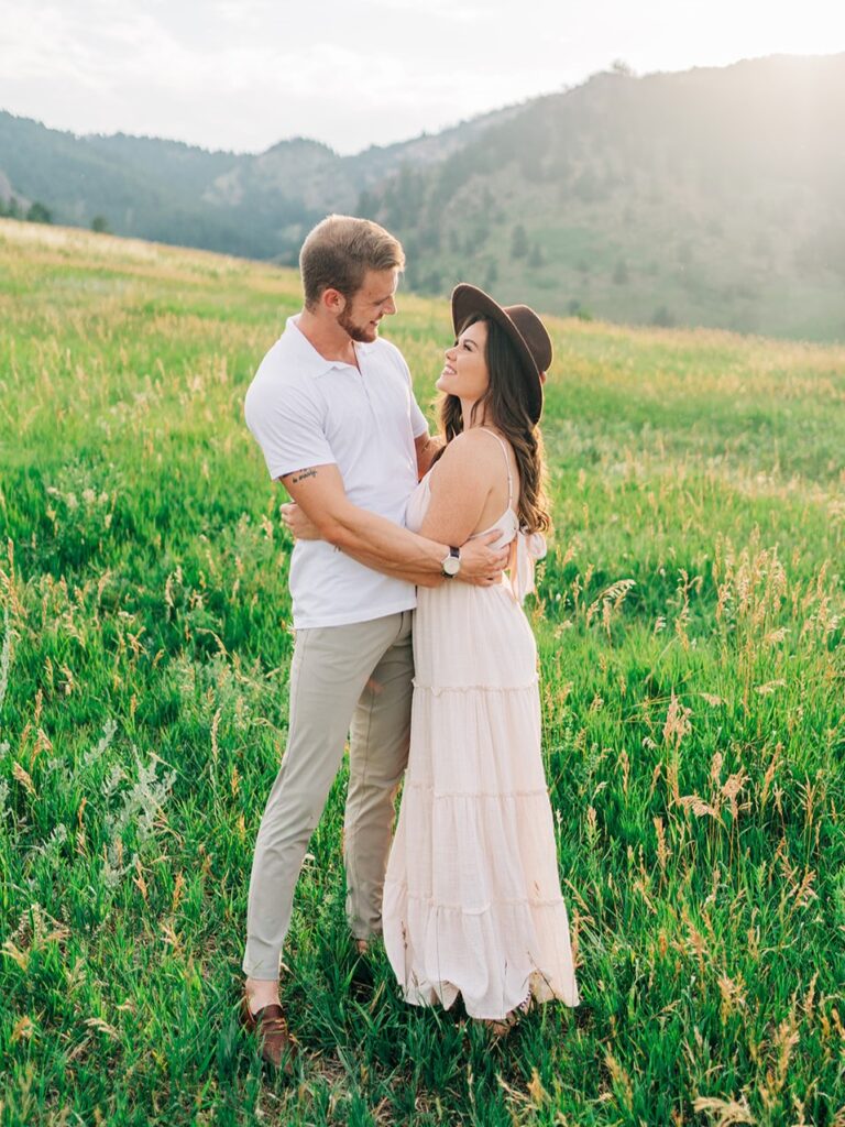 couple holding on to each other and smiling in a grassy field at chautauqua park during their boulder colorado couples photoshoot