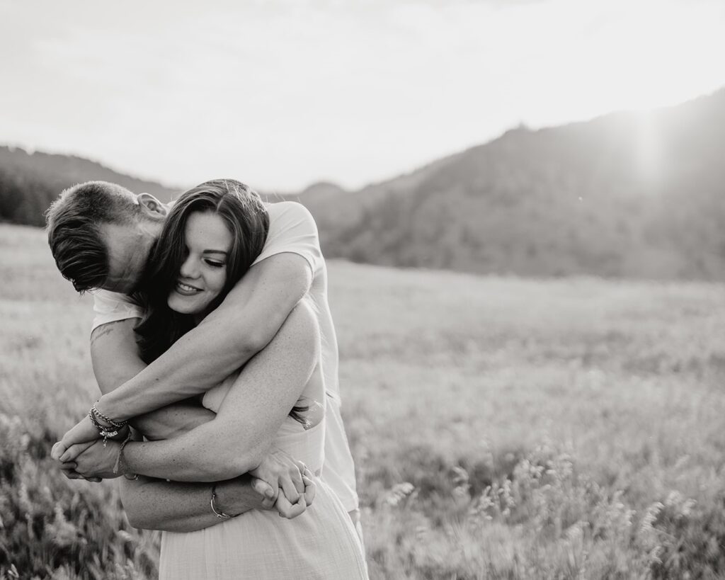 boyfriend and girlfriend all wrapped up and snuggly while he kisses her on the temple during their boulder colorado couples session at chautauqua park