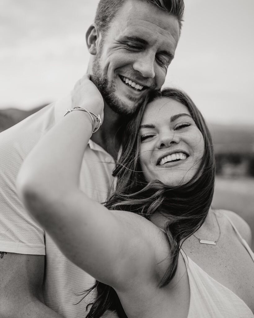 girlfriend holding her boyfriends face as they laugh and smile at the camera during their couples session in boulder colorado at chautauqua park