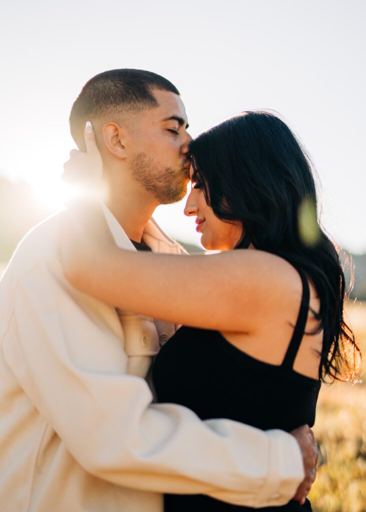 boyfriend kissing his girlfriends forehead while the sun shines in the background at lost gulch overlook during their couples photoshoot