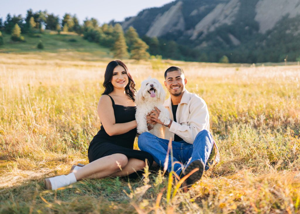 cute latina couple sitting a field with their dog at Chautauqua park in boulder colorado during their couples photoshoot