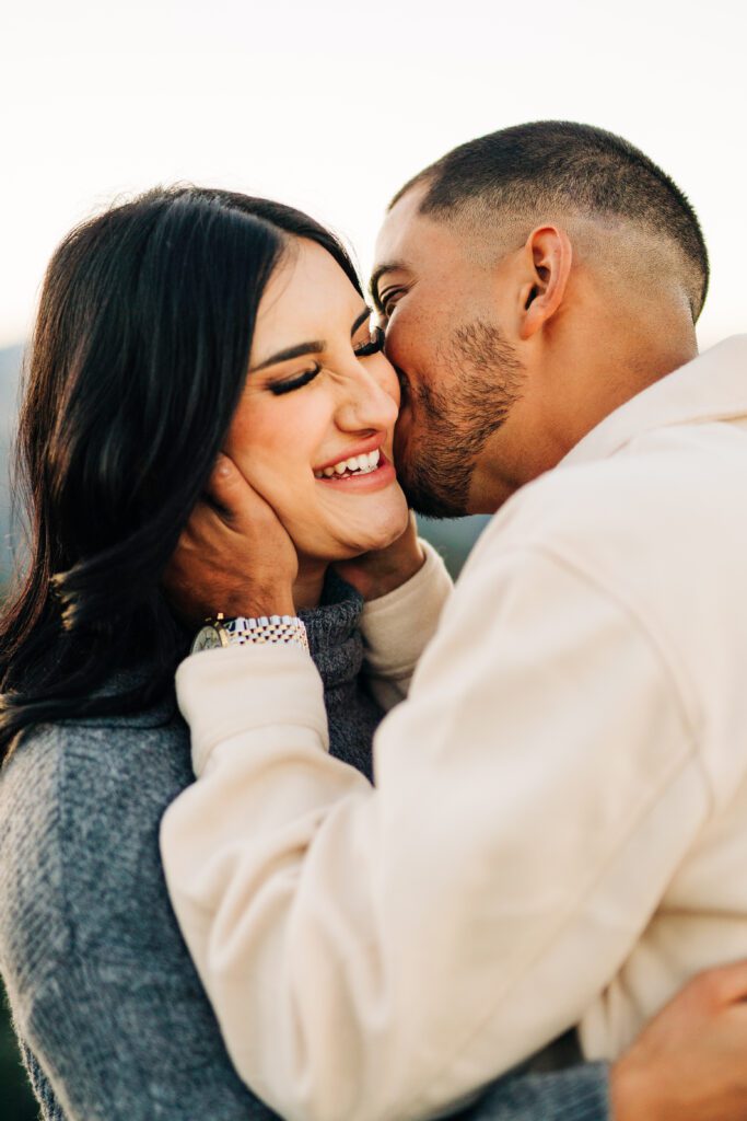 girl smiling as her boyfriend kisses her all over her face at lost gulch overlook in boulder colorado during their couples photoshoot