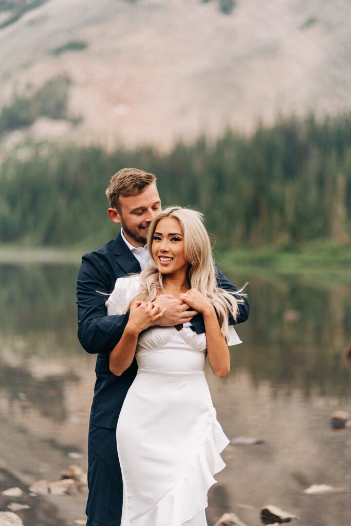 Groom kissing the bride on the head while she smiles at the camera with Lake Mitchell in the background during their Colorado Elopement at Brainard Lake Recreation Area