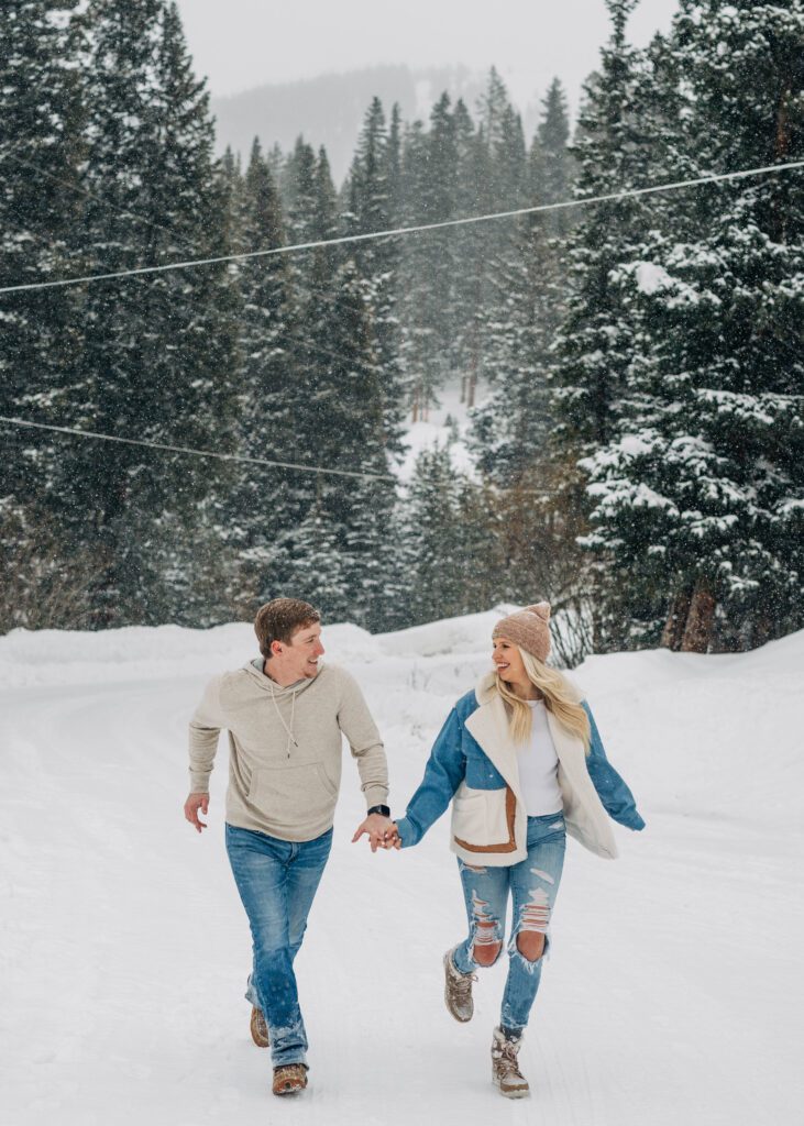 cute couple holding hands and running towards the camera in the snow during their breckenridge engagement session