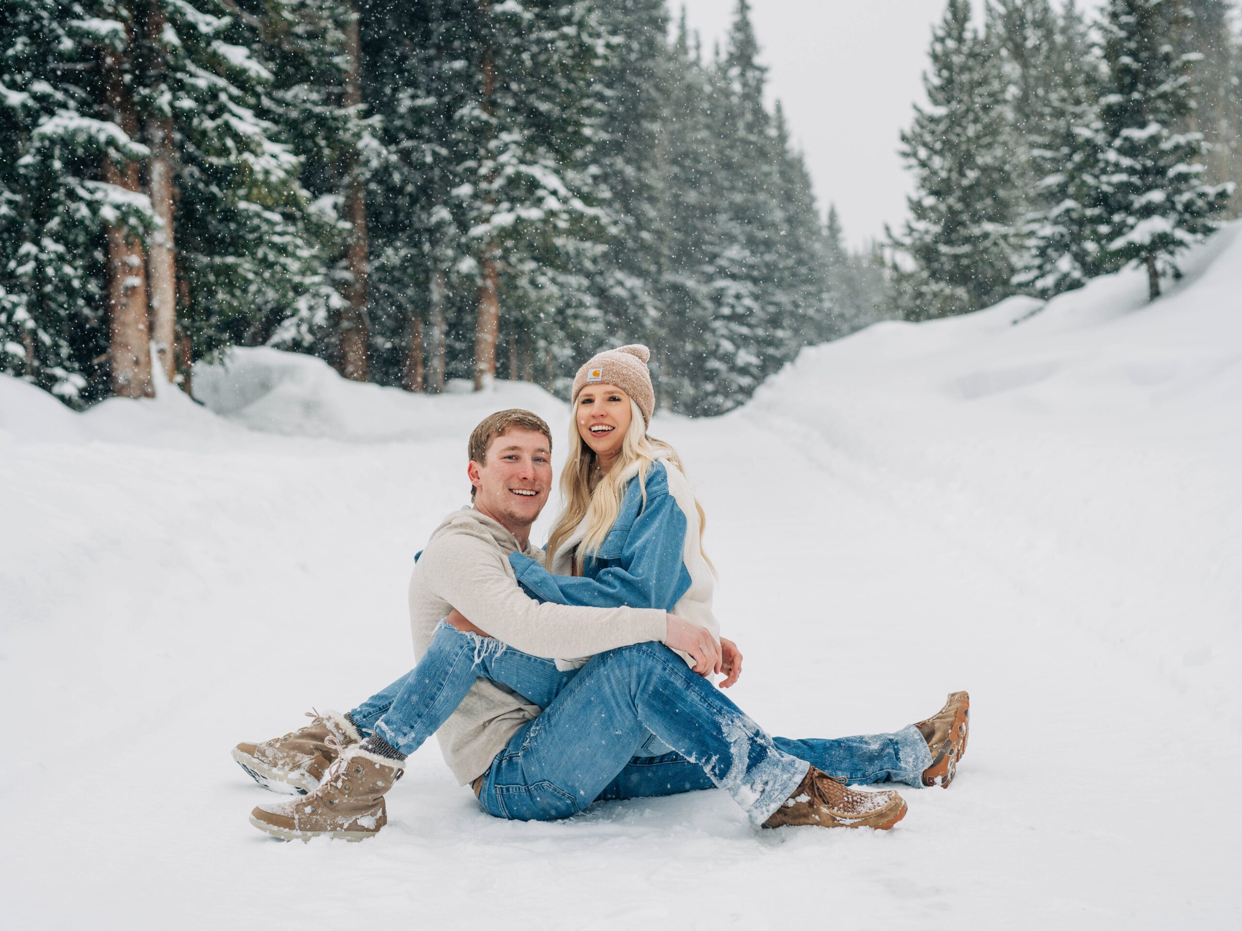 cute couple sitting in the snow smiling at the camera during their breckenridge engagement session