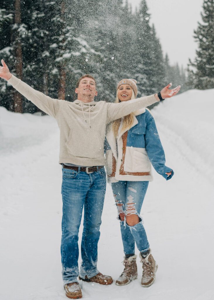 boyfriend throwing snow up in the air as girlfriend watches during snowy engagement session in breckenridge colorado