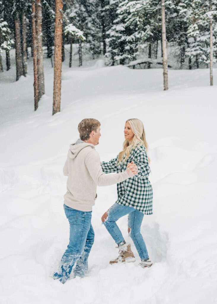 cute couple holding hands and spinning eachother around in the snow during their breckenridge engagement session