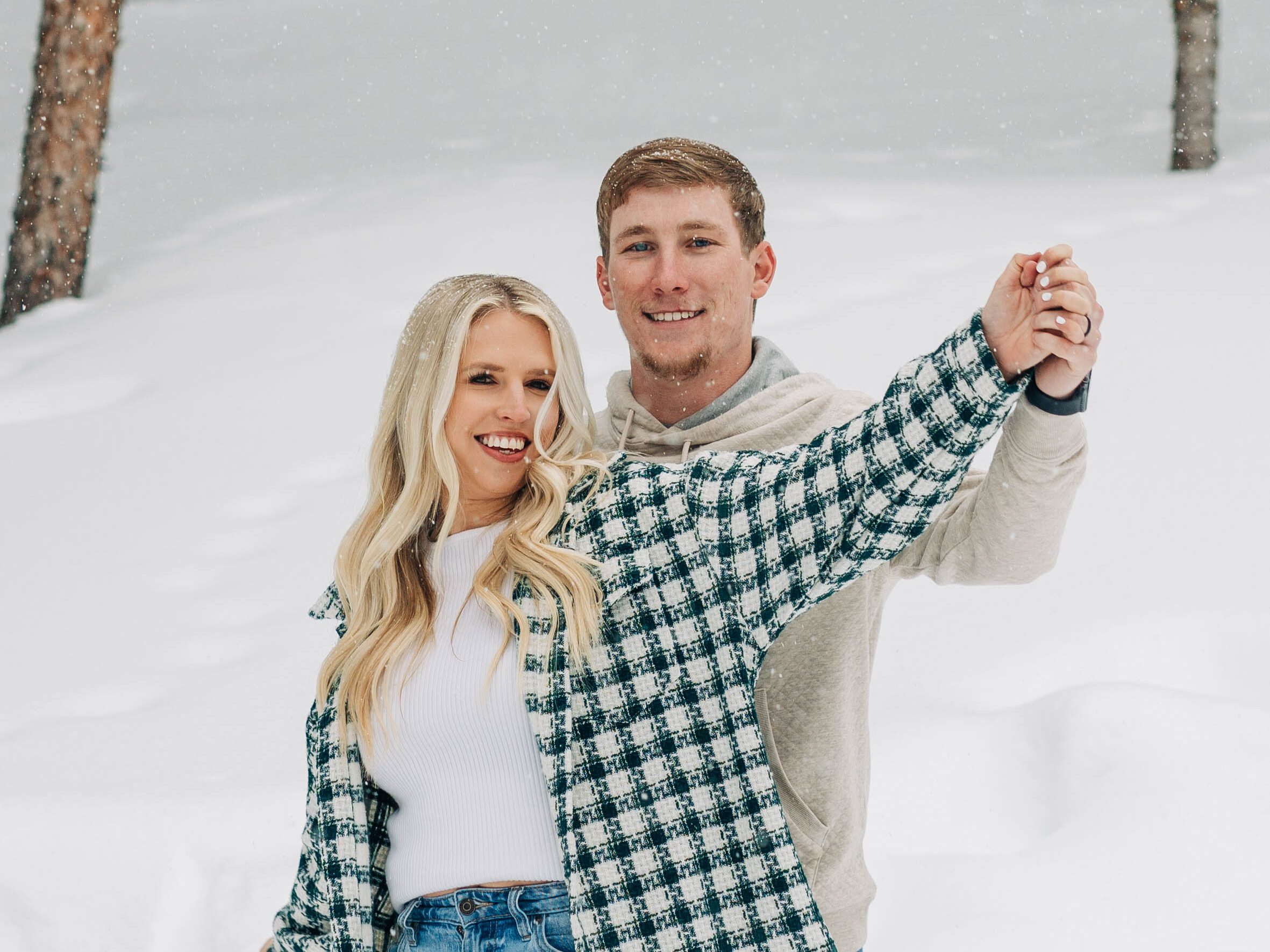 cute couple holding hands and smiling at the camera doing airplane arms in the snow during their breckenridge engagement session