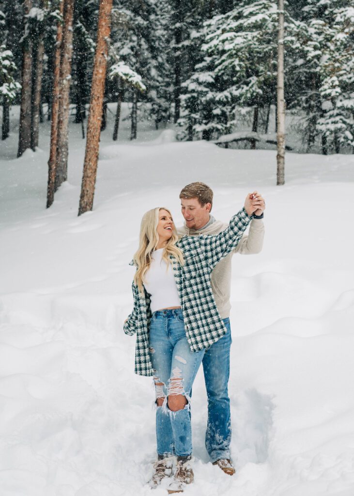 engaged couple standing in the snowing smiling at each other while doing airplane arms during their breckenridge engagement session
