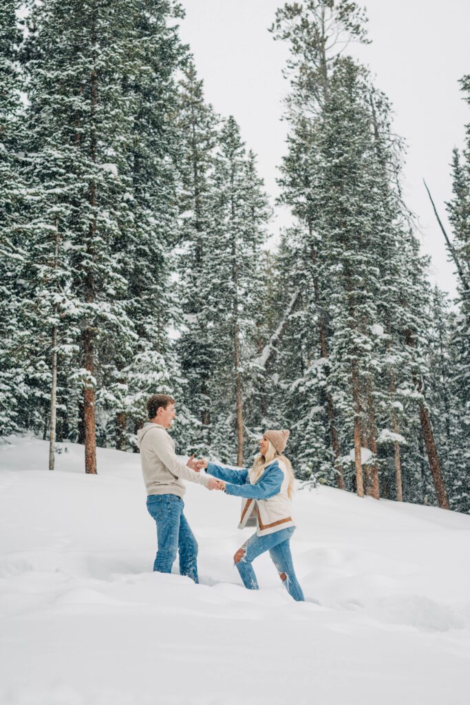 boyfriend helping girlfriend walk up snowy hill during their breckenridge engagement session