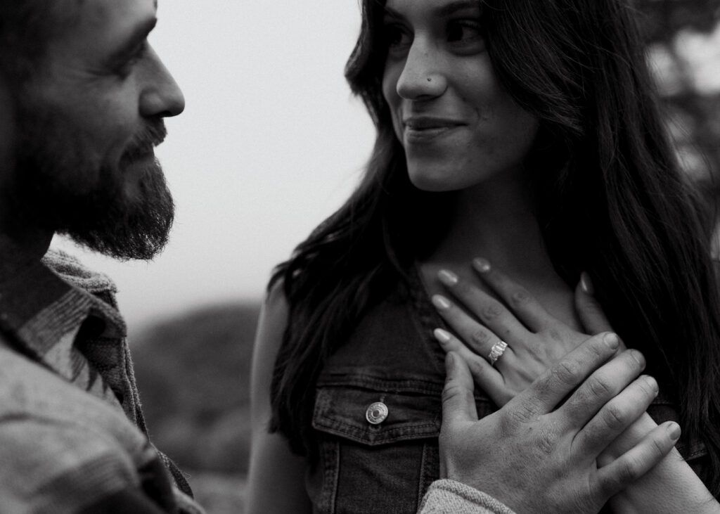 fiance holding his hand to his girl friends chest smiling at each other during their proposal photoshoot in colorado
