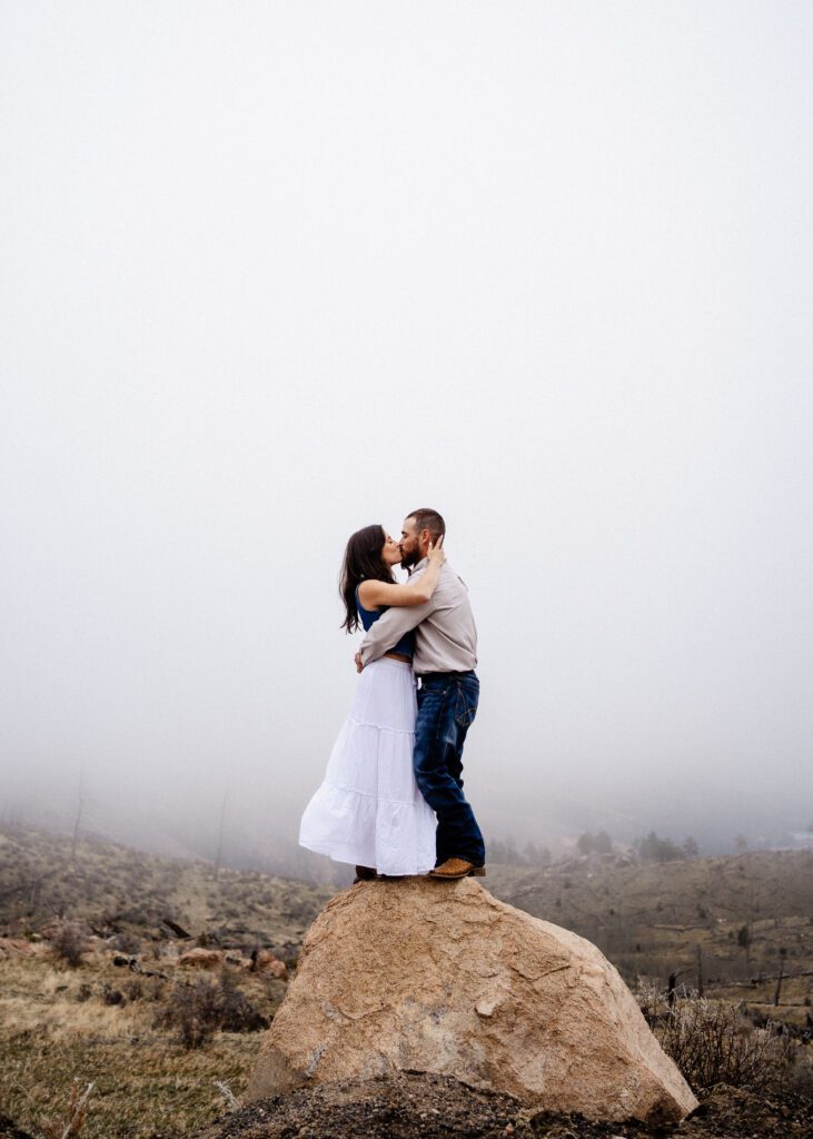 engaged couple standing on a rock kissing in the middle of field during a storm in colorado