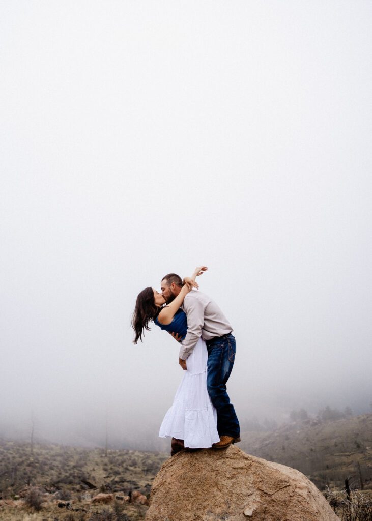newly engaged couple standing on a rock kissing while he leans her back during their proposal in colorado