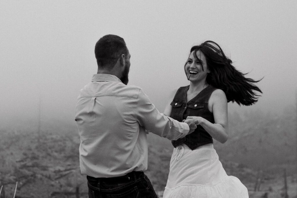 newly engaged couple holding hands and spinning around smiling during their proposal in colorado