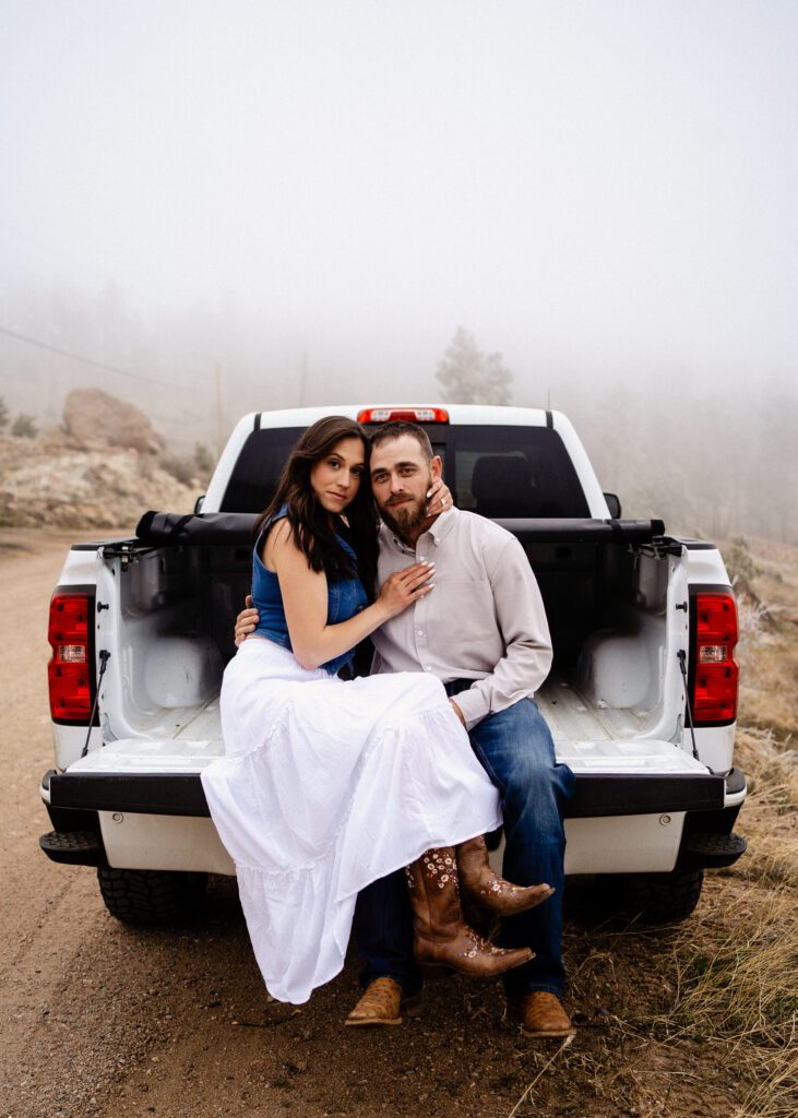 engaged couple sitting on the tailgate of a pickup truck during their proposal in colorado
