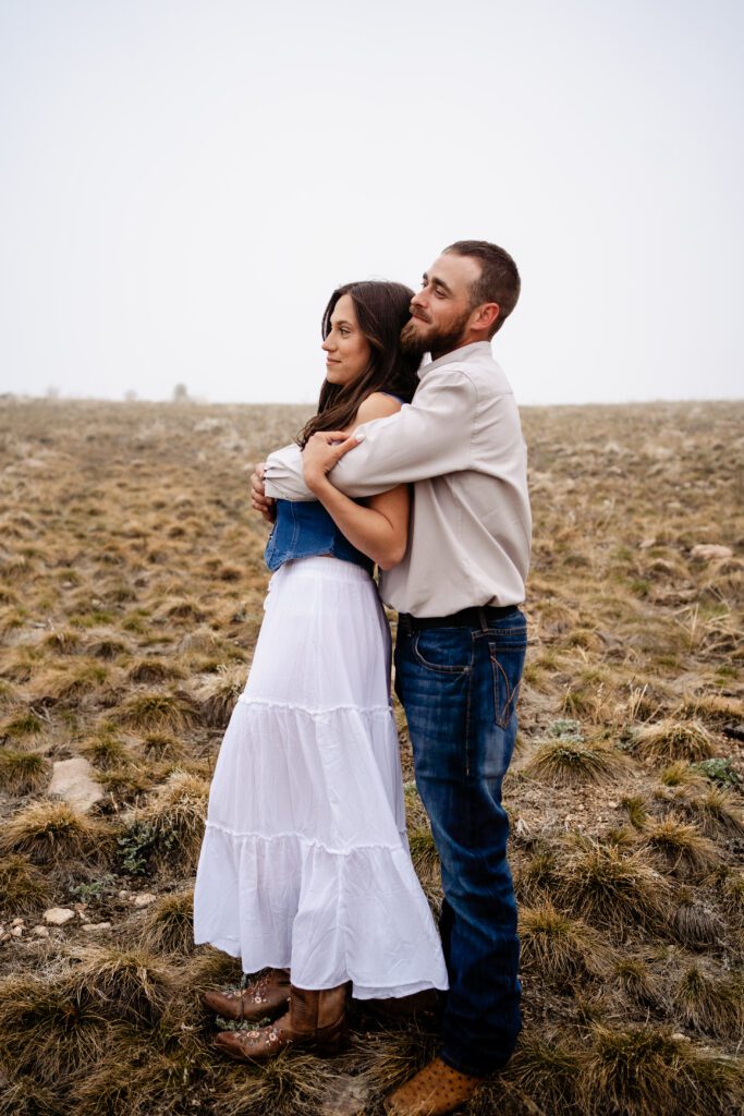 newly engaged couple standing in a field looking out in the distance together during their proposal session in colorado