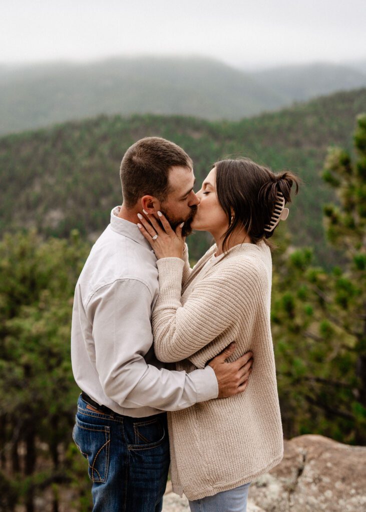 newly engaged couple kissing with the mountains in the background during their proposal in colorado