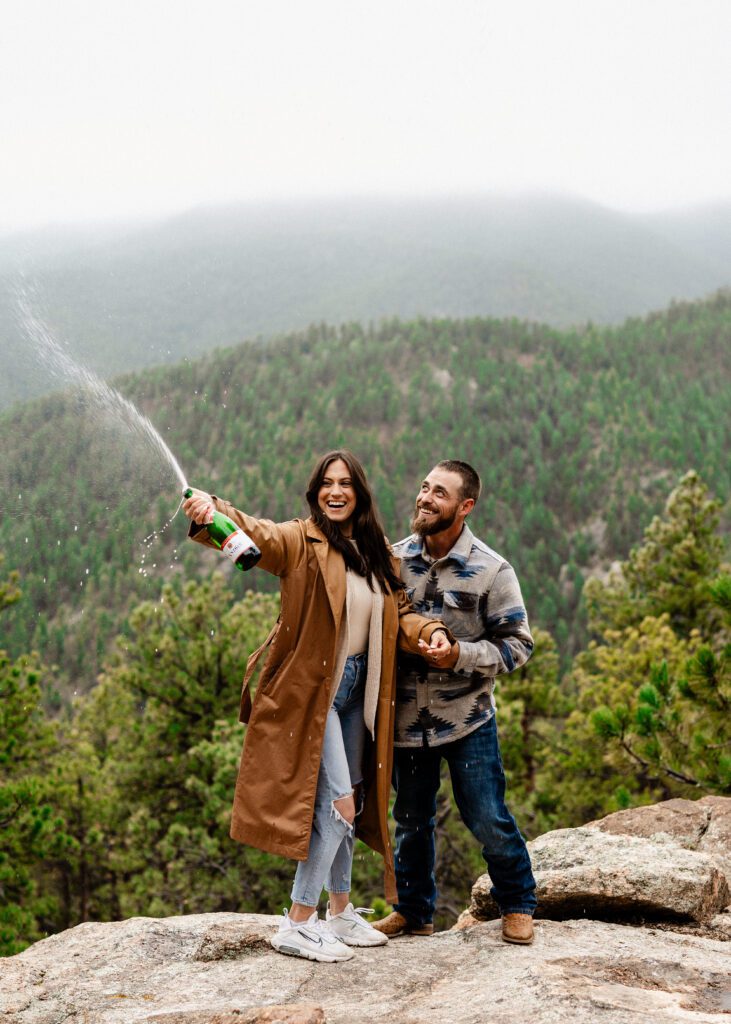 engaged couple spraying champagne on the side of a mountain during their proposal in colorado